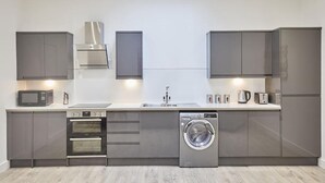Une cuisine moderne dotée d’appareils électroménagers intégrés, notamment un four à micro-ondes, un four et un lave-linge, et de meubles de rangement gris.