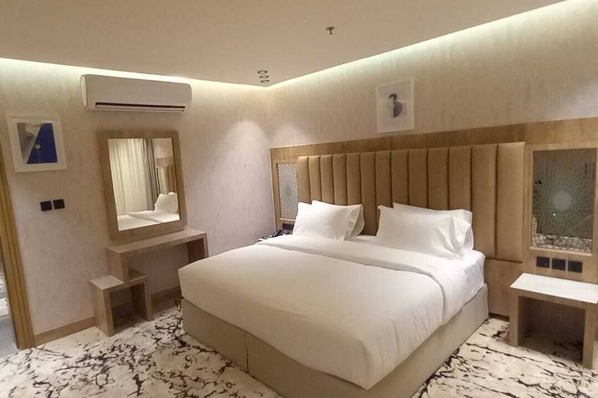 A hotel room with a large bed, a bedside table, a mirror, and an air conditioning unit.