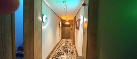 A hotel hallway with a patterned carpet, wooden walls, and a door at the end.