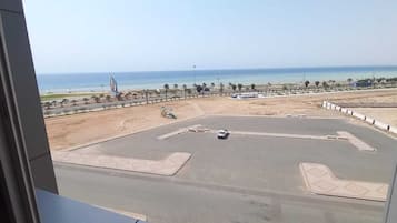 Vista da janela sobre um parque de estacionamento, com uma praia ao fundo.