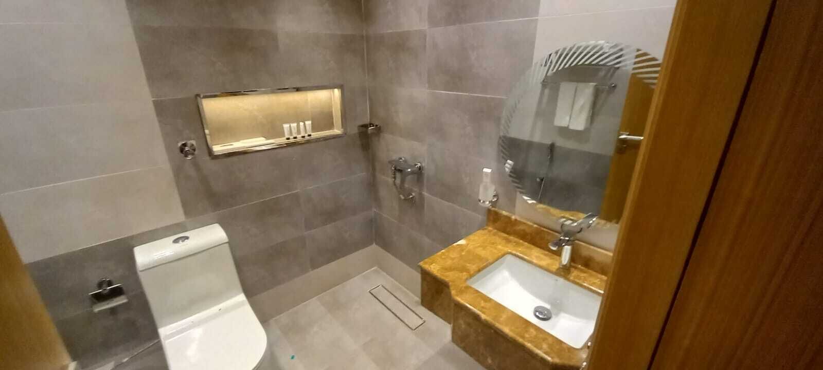 A bathroom with a toilet, sink, mirror, and shower.