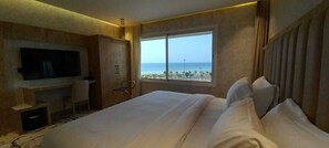 Habitación de hotel con una cama grande, televisor montado en la pared, armario y ventana con vista a la playa y al océano.