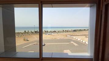 Vista des d'una finestra sobre una platja, amb una zona d'aparcament i un cel serè.
