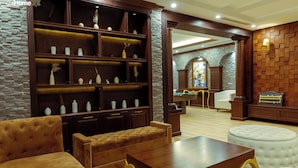 Un amplio salón con una gran estantería de madera, un sofá capitoné, una mesa de centro y un otoman blanco.