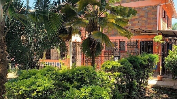 A two-story building with a brick facade, a gated entrance, and lush greenery including palm trees and shrubs. - Torchys Lounge  Hotel in Kisumu Unit 2 (Kisumu)