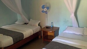 Una habitación con dos camas, una mesita de noche con un ventilador y una botella de agua.