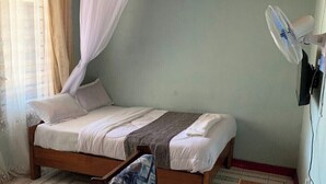 Una cama individual con dosel, un ventilador de pie y un televisor montado en la pared.