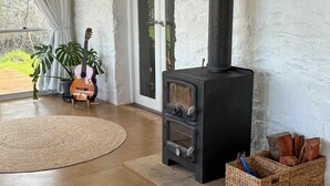 A cozy living room with a black wood-burning stove, a guitar, and potted plants. - Breathe Holiday Retreat - 107 Nettle Hill Rd, Hind (Hindmarsh Valley)