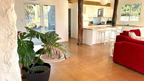 A modern living room with a red sofa, a kitchen area with white cabinets, and a large potted plant. - Breathe Holiday Retreat - 107 Nettle Hill Rd, Hind (Hindmarsh Valley)