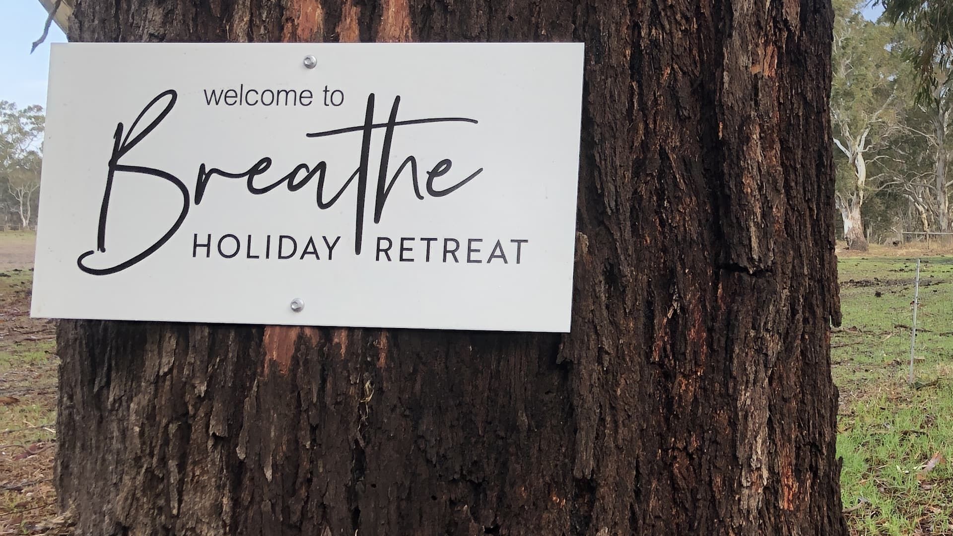 Een bord aan een boom met de tekst 'welcome to Breathe HOLIDAY RETREAT'.