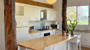 A modern kitchen with white cabinets, a wooden countertop, and a large window offering a view of trees. - Breathe Holiday Retreat - 107 Nettle Hill Rd, Hind (Hindmarsh Valley)