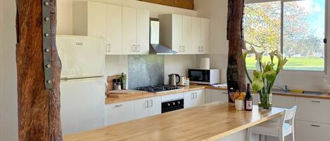 A modern kitchen with white cabinets, a wooden countertop, and a large window offering a view of trees.