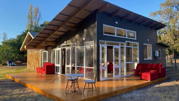 A modern house with a wooden deck, large glass windows, and red outdoor furniture. - Breathe Holiday Retreat - 107 Nettle Hill Rd, Hind (Hindmarsh Valley)