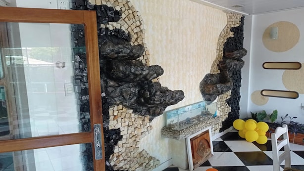 A room with a checkered floor, a glass door, a wall with a rock and mosaic design, and a small shelf with yellow and orange balloons. - OYO Hotel Tbs (Manacapuru)