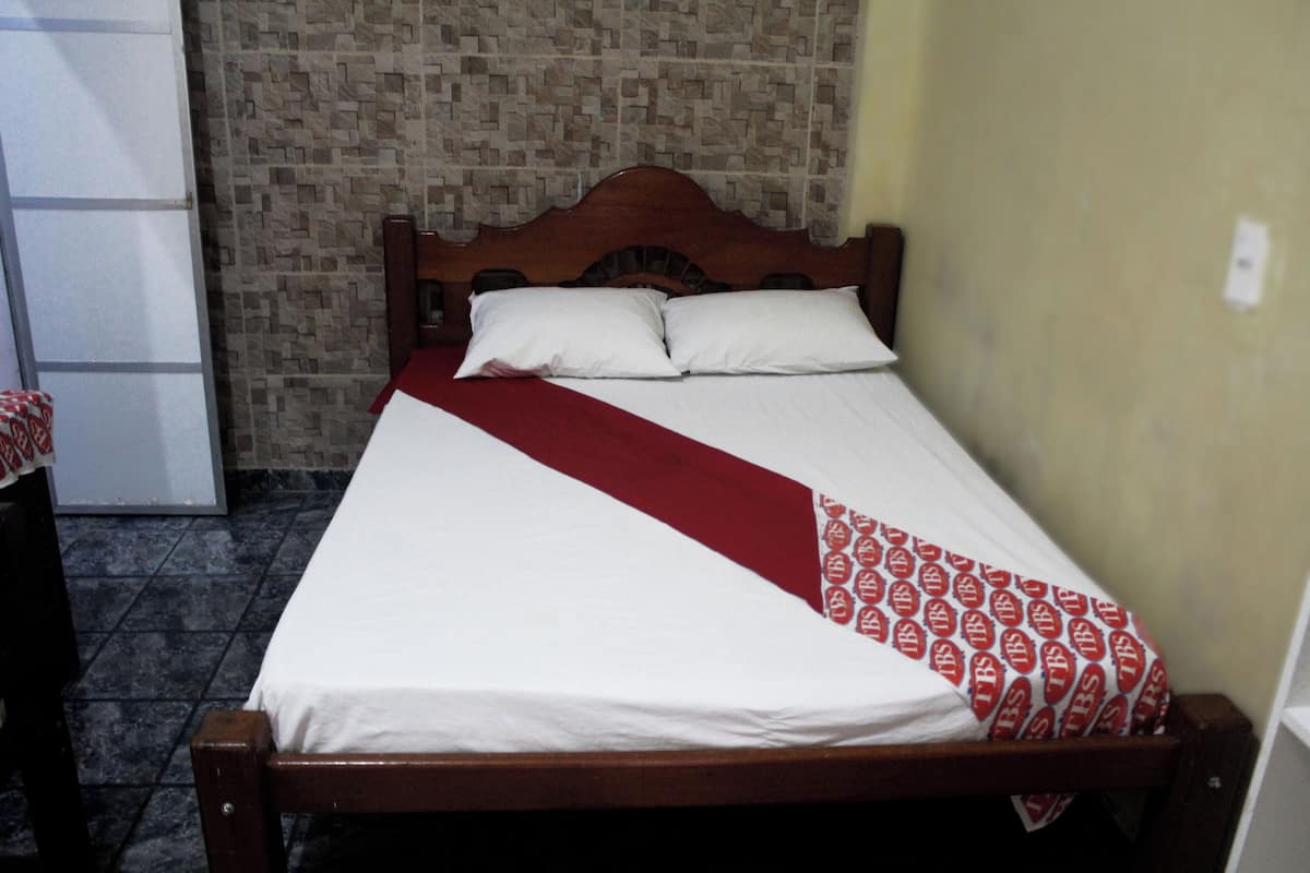Un lit avec une tête de lit en bois, une literie blanche et une couverture à motifs rouges et blancs.