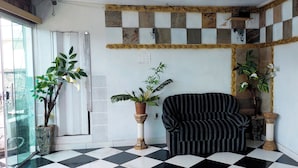 A corner room with a checkered floor, a striped armchair, and two potted plants. - OYO Hotel Tbs (Manacapuru)