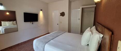 A hotel room with a large bed, a flat-screen TV mounted on the wall, a door with a fish-shaped mirror, and a light fixture above the bed.