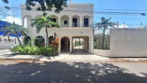 A two-story building with a gated entrance, surrounded by palm trees and a concrete wall. - Capital O Hotel Rolovi Cancún (Cancun)