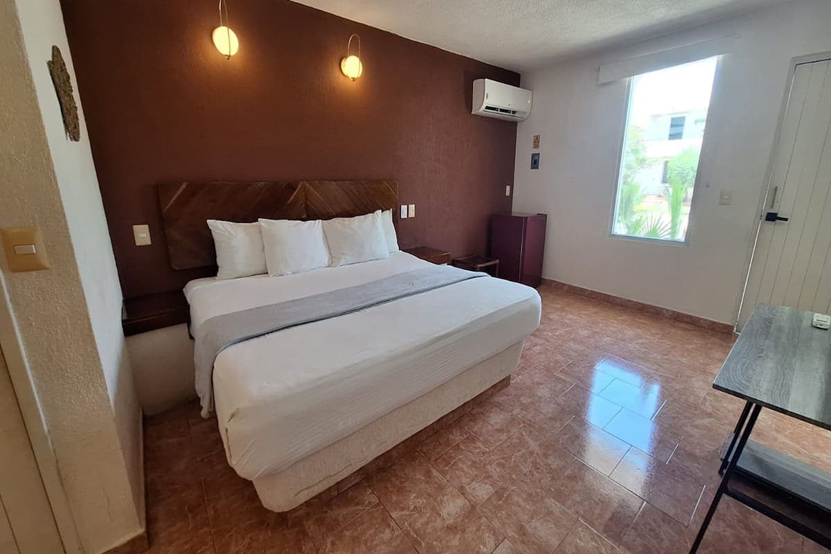 A bedroom with a large bed, a nightstand, a dresser, a window with a view, and an air conditioning unit.