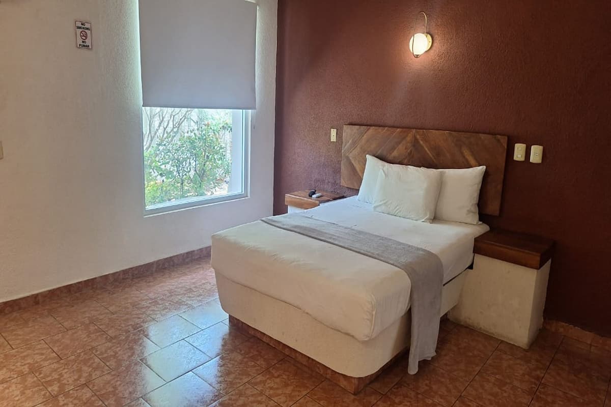 A bedroom with a bed, nightstands, a window, and a wall-mounted light fixture.