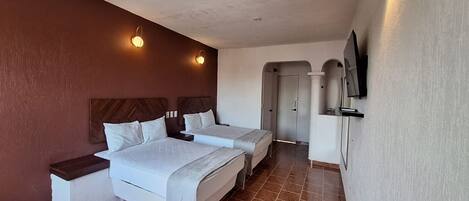 Una habitación de hotel con dos camas, un televisor montado en la pared y una puerta que da a otra estancia.
