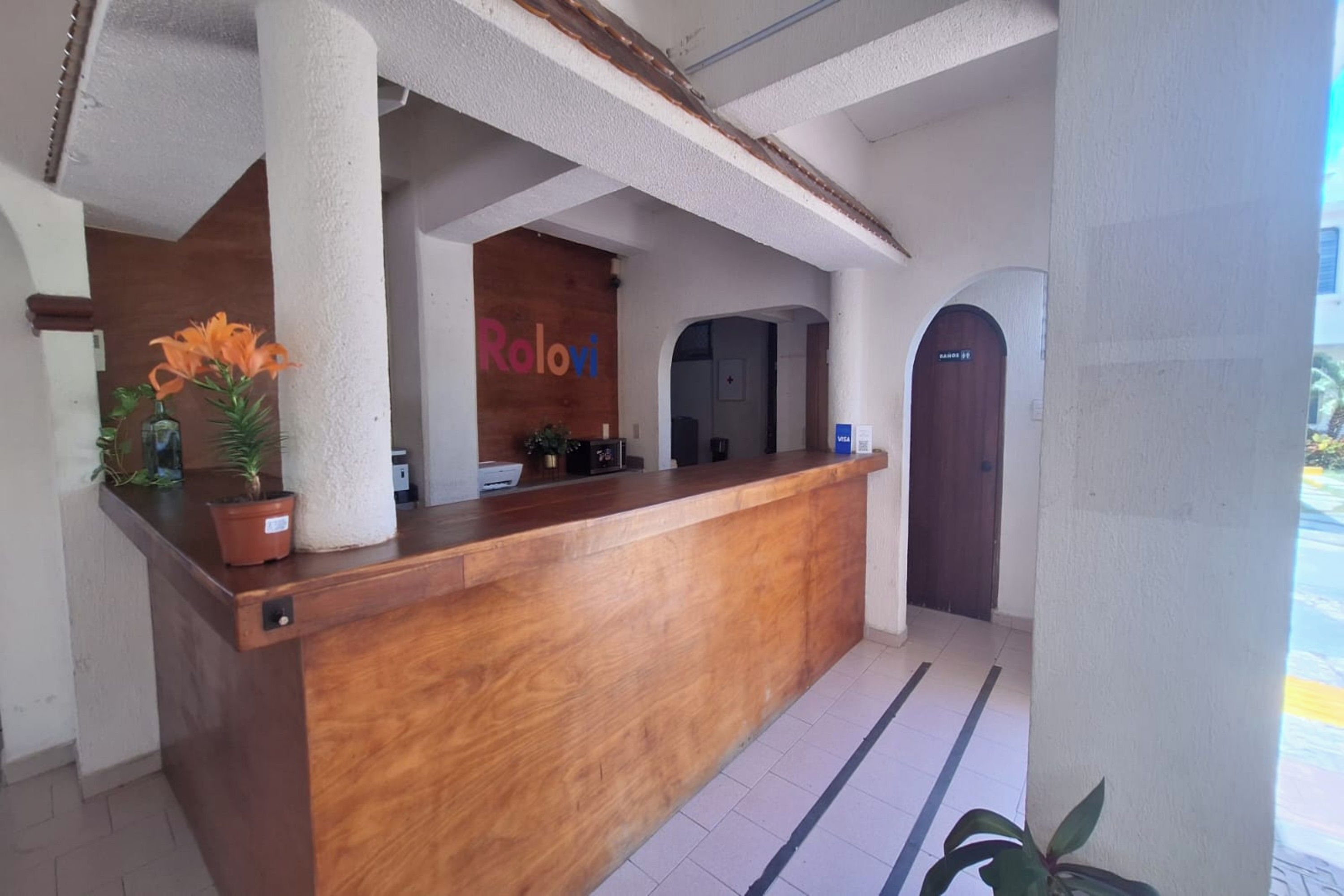Un mostrador de recepción con encimera de madera, un cartel que dice 'Rolovi' y una puerta con un letrero que indica 'BAHOS'.