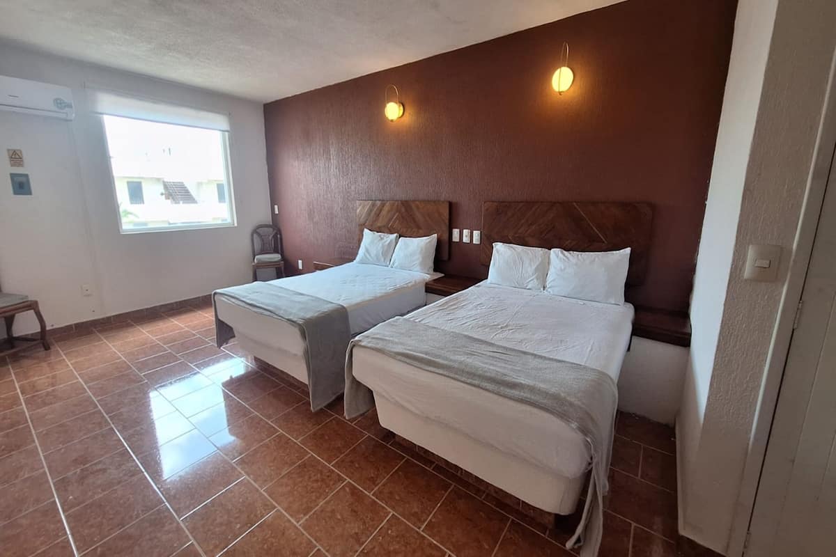 A hotel room with two beds, a window, and a chair.