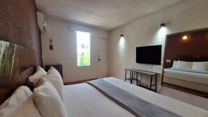 A hotel room with a large bed, a desk, a flat-screen TV mounted on the wall, and a window with a view of greenery. - Hotel Rolovi Cancun (Cancun)
