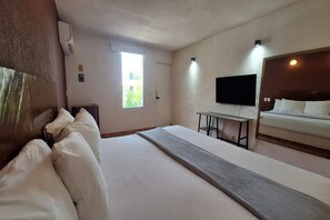 A hotel room with a large bed, a desk, a flat-screen TV mounted on the wall, and a window with a view of greenery. - Hotel Rolovi Cancun (Cancun)
