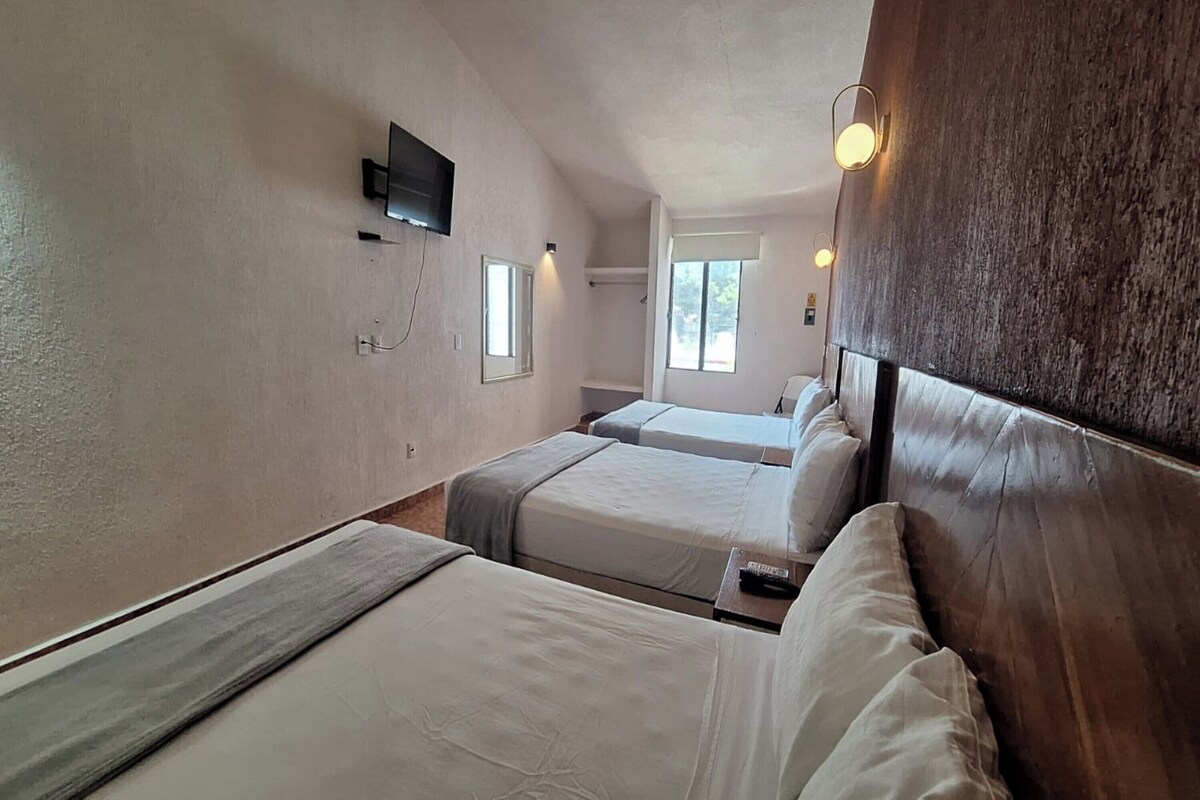 A room with two beds, a television mounted on the wall, and a window with a view of the outside.