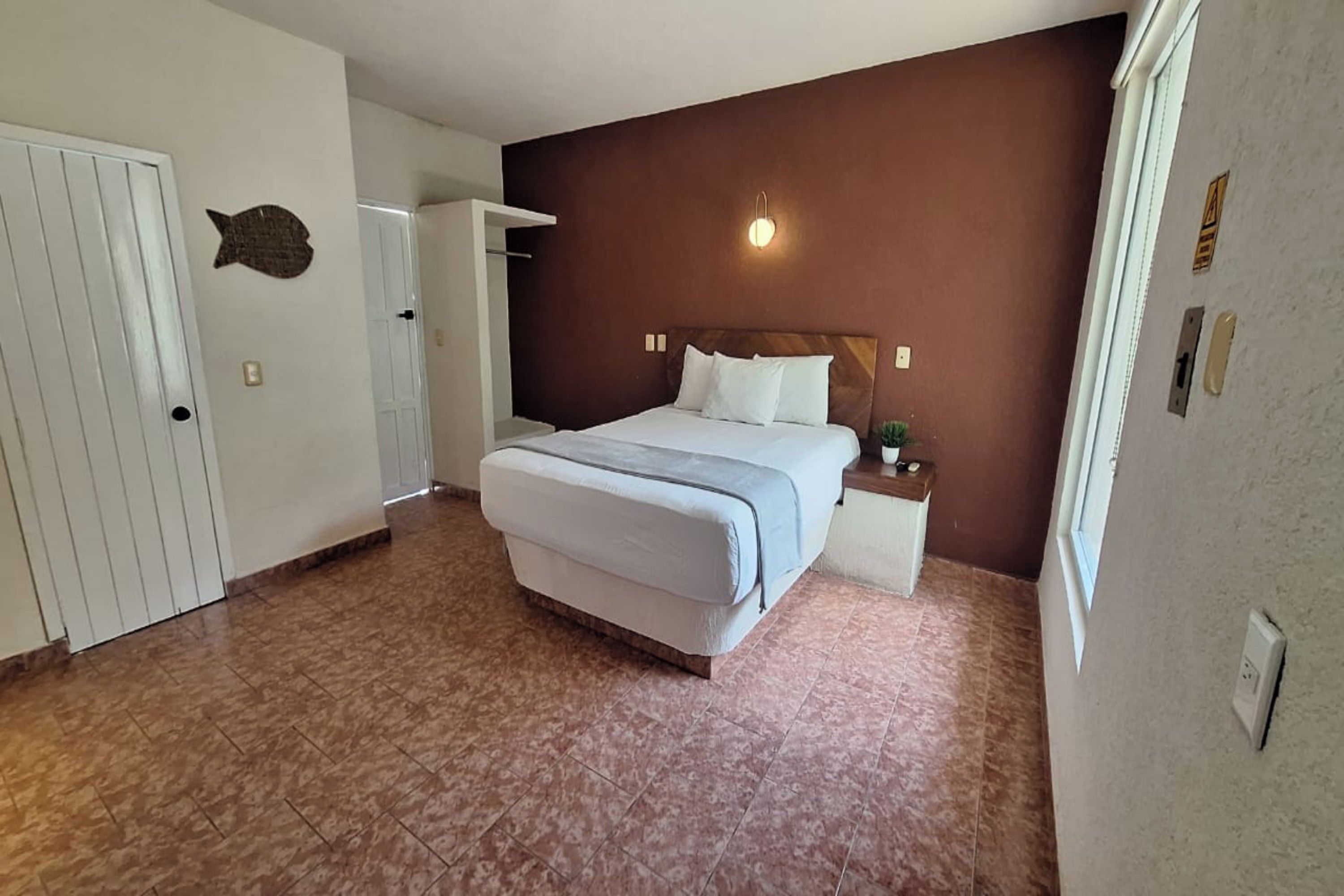 A bedroom with a bed, a nightstand, a wall-mounted light, a door, and a fish decoration.