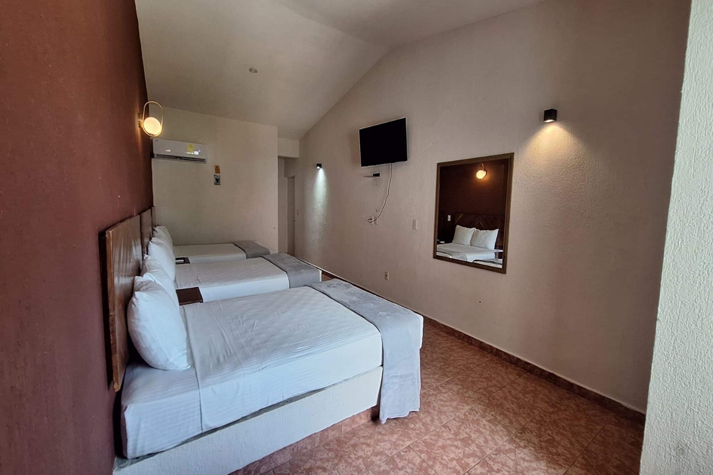 A hotel room with two beds, a television mounted on the wall, and a small mirror above the beds.