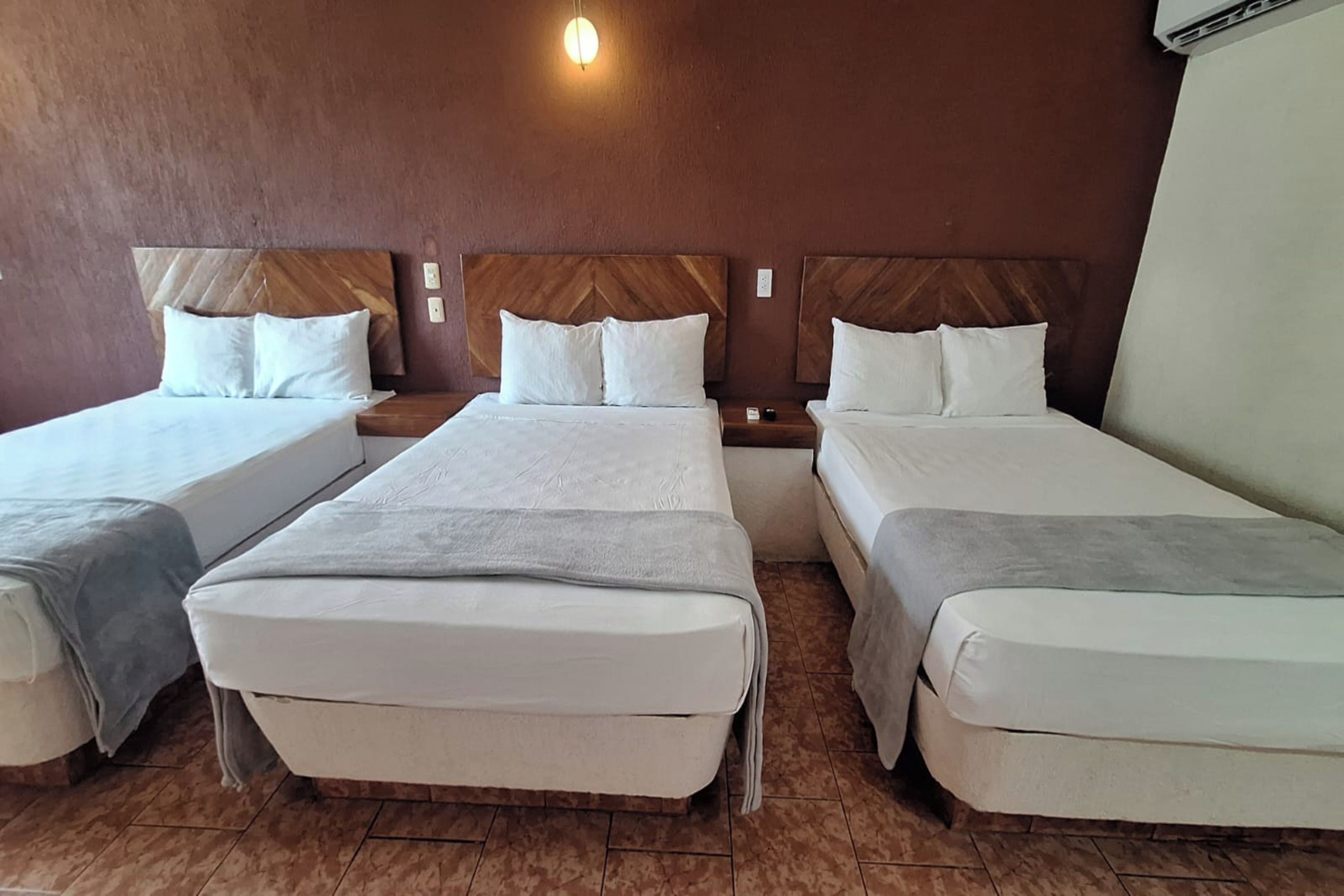 A hotel room with three beds, wooden headboards, and a light fixture on the ceiling.