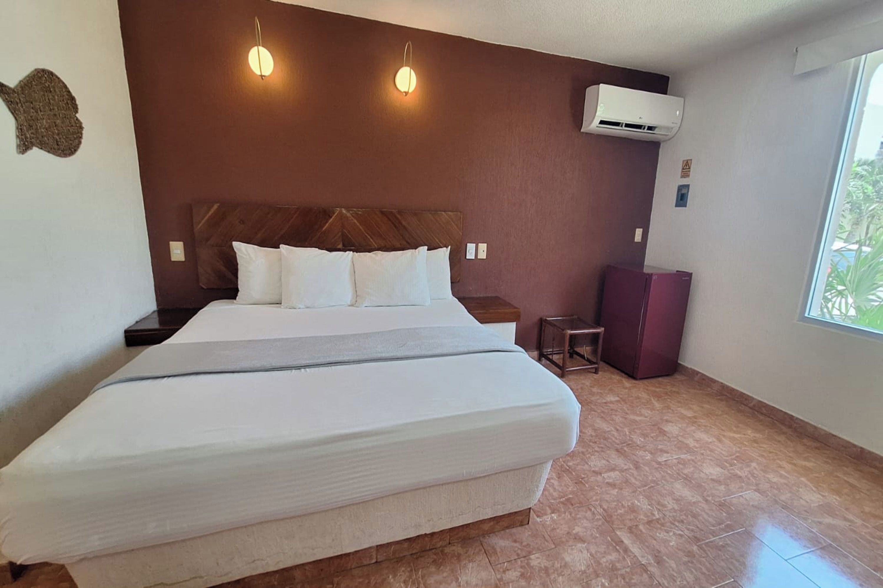 Une chambre d’hôtel avec un grand lit, deux lampes fixées au mur, un climatiseur, une petite table et un placard.