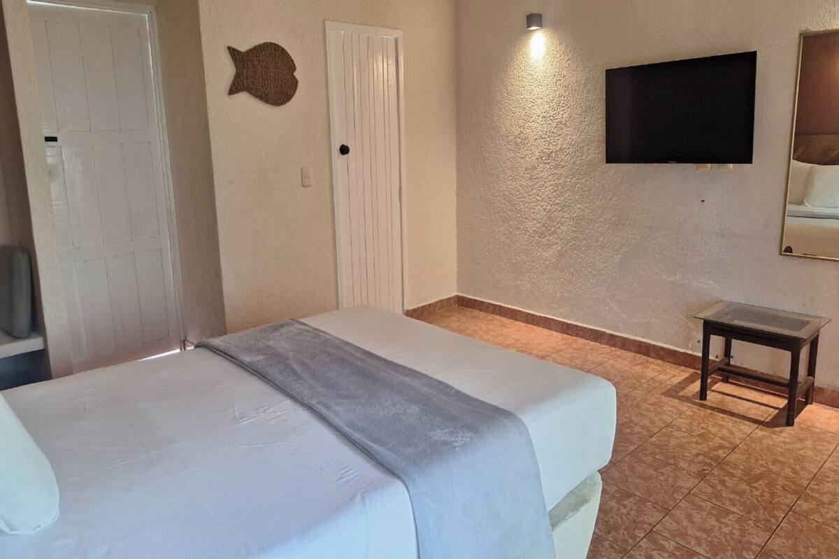 A hotel room with a bed, a television mounted on the wall, a small table, and a door.