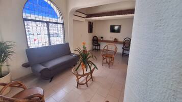 A living room with a sofa, chairs, a coffee table, a TV, and a large window with a view of the street.