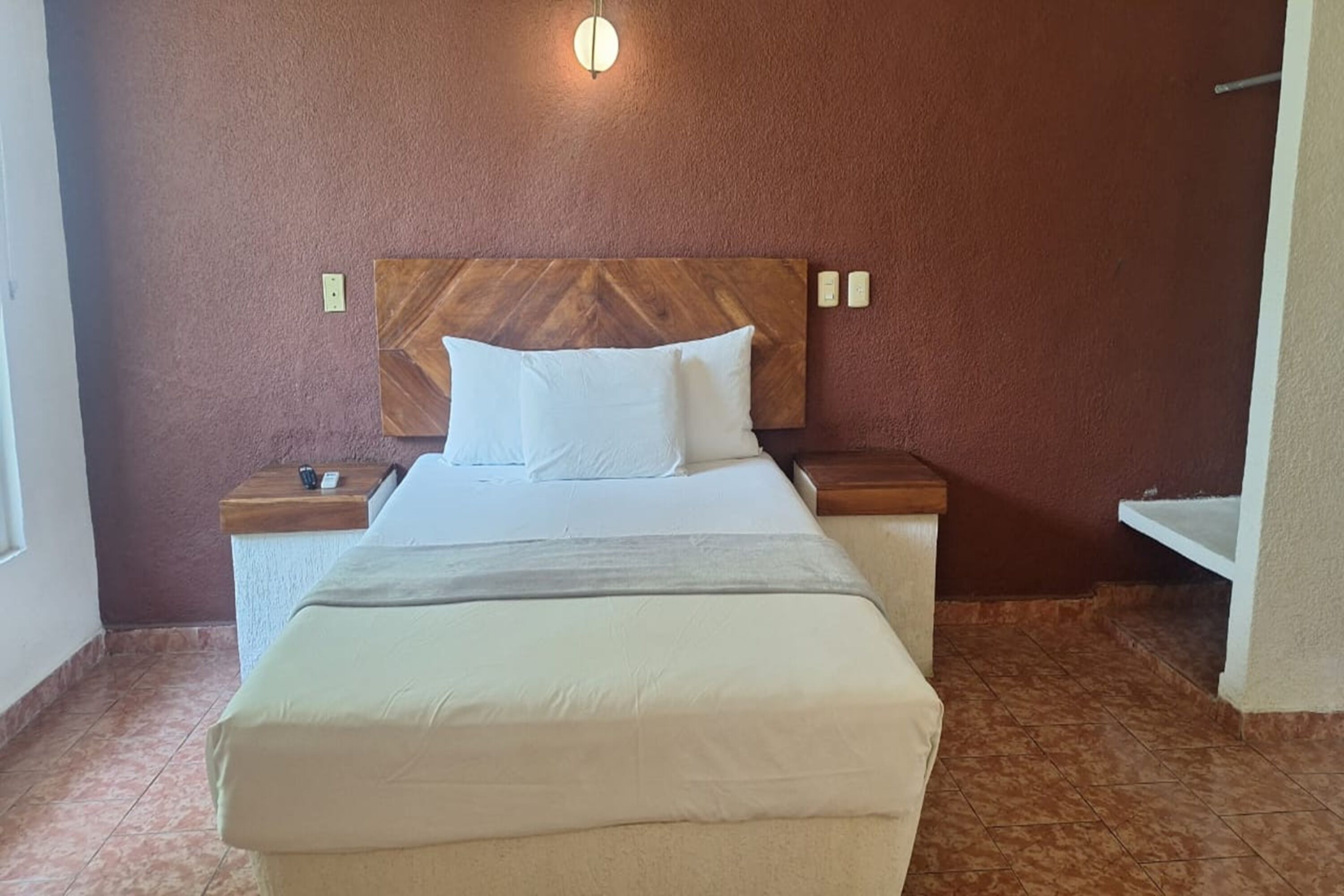 A neatly made bed with a wooden headboard, a bedside table with a lamp, and a wall-mounted light fixture.