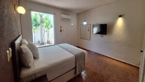 A hotel room with a bed, a window with a view of palm trees, an air conditioner, a flat-screen TV mounted on the wall, and a door. - Capital O Hotel Rolovi Cancún (Cancun)