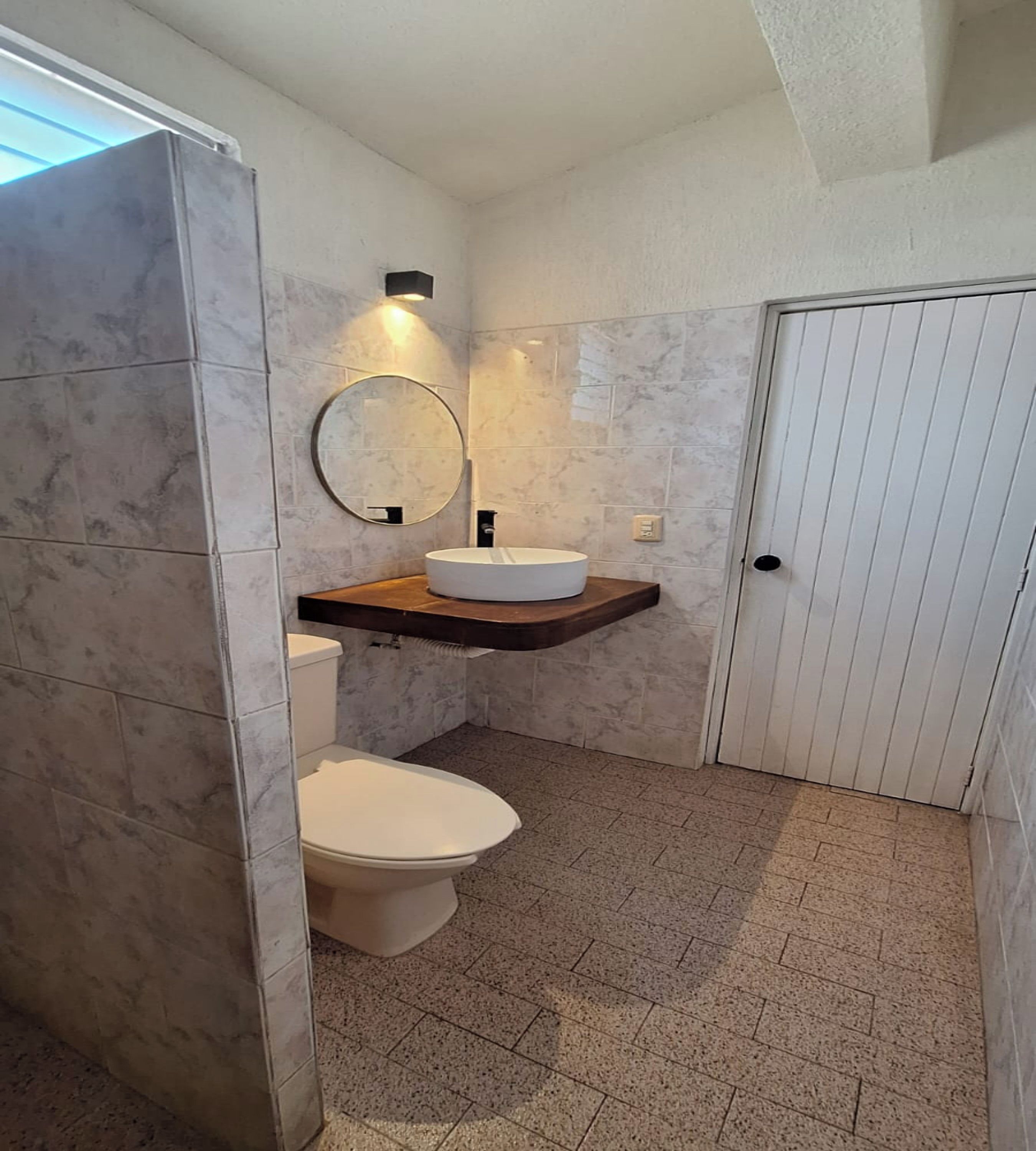 Une salle de bain avec des toilettes, un lavabo avec un miroir et une porte.