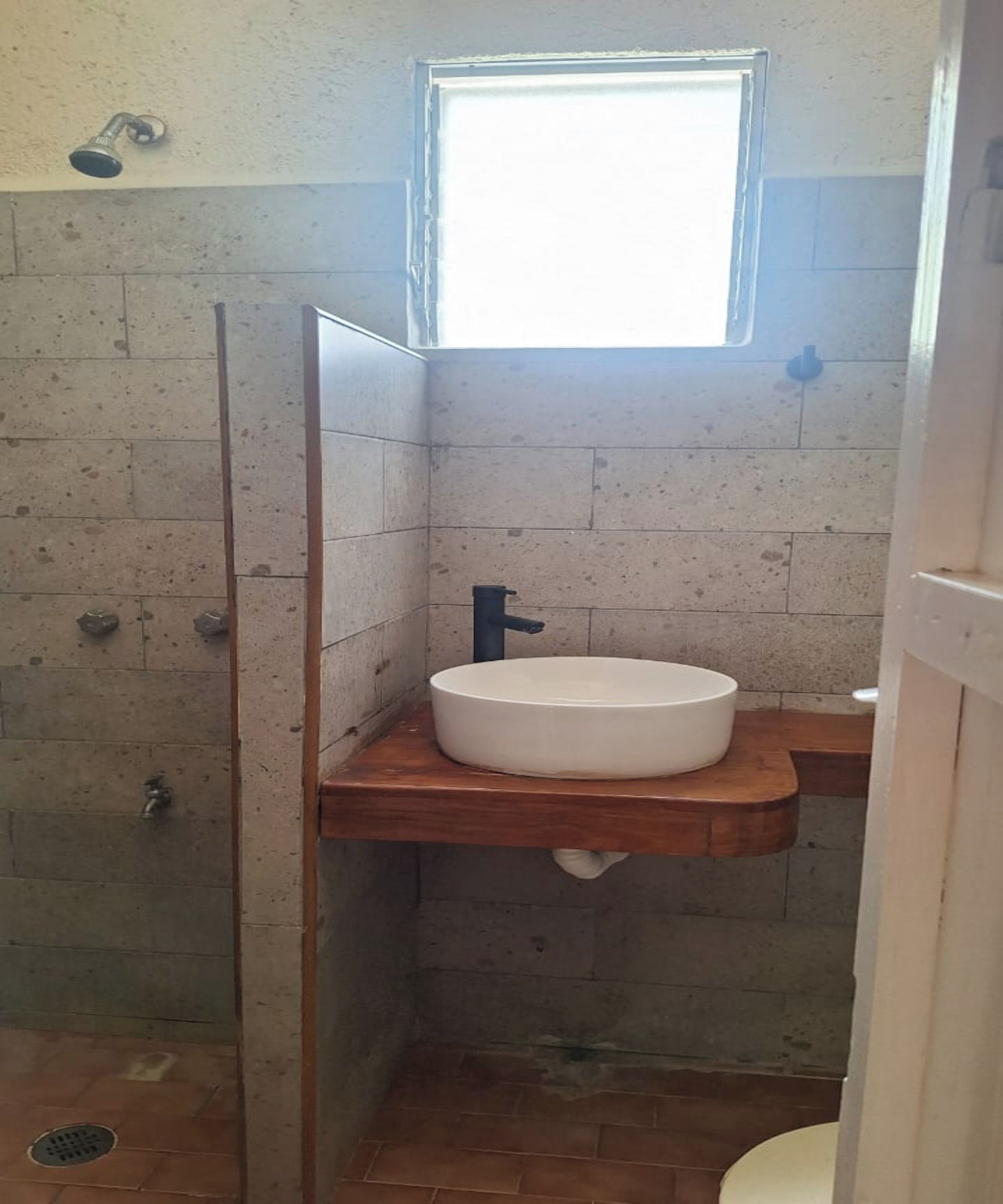 A small bathroom with a shower, a sink, and a window.
