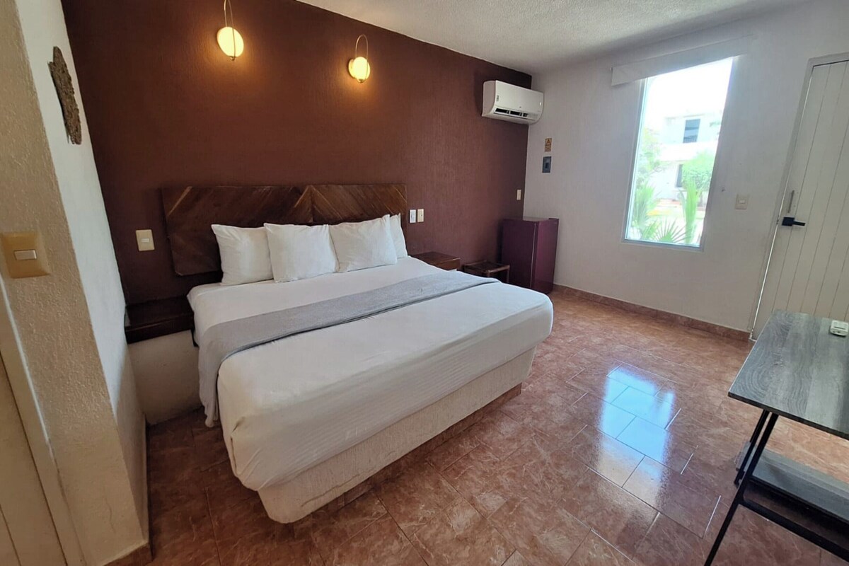 A bedroom with a bed, two bedside tables, a window, and an air conditioning unit.