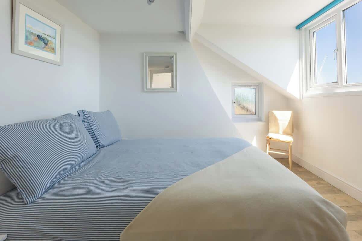 Un dormitorio con cama, una silla, una ventana y un cuadro en la pared.