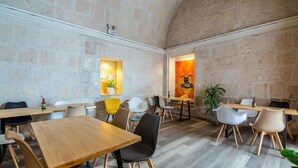 A modern dining area with wooden tables and chairs, a stone wall, and a plant. - Hotel Mosna (Arequipa)