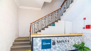 A hotel reception desk with a geometric patterned wall, a staircase with a wooden handrail, and a potted plant. - Hotel Mosna (Arequipa)