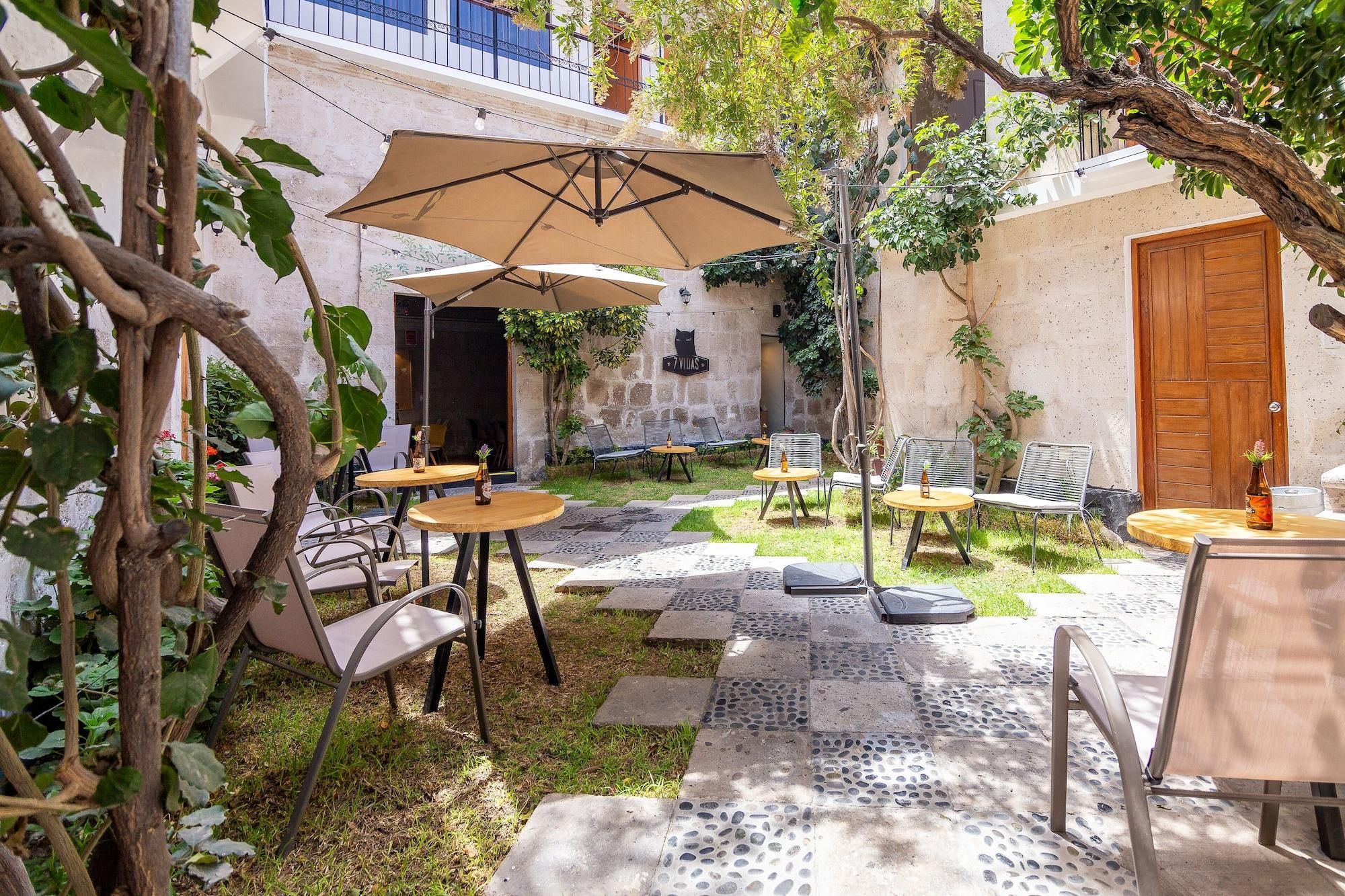 Terrassa a l'aire lliure amb taules i cadires, envoltada de vegetació i un mur de pedra.