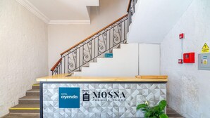 A hotel reception desk with a geometric-patterned wall, a staircase with ornate railings, and a potted plant. - Hotel Mosna (Arequipa)