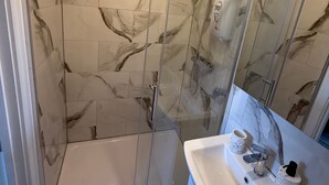 Ein Badezimmer mit einer gläsernen Duschkabine, Marmorfliesen, einem Waschbecken mit Spiegel und einem Halter für Tassen.