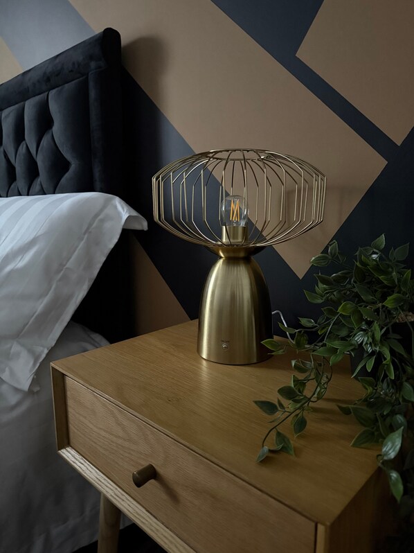 A bedside table with a brass lamp, a drawer, and a potted plant.