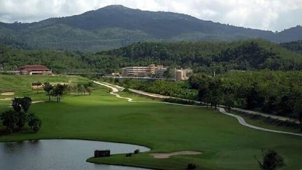 A golf course with a pond, a building, and a mountain in the background.
