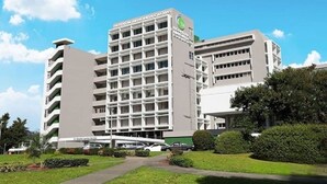 A multi-story hospital building with a modern design, featuring a central courtyard with pathways and greenery.